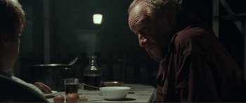 Movie still from “Adoration” (2019), directed by Fabrice du Welz – An older man sitting at a table with a bowl of food; Medium shot, Over the shoulder angle