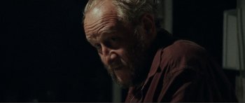 Movie still from “Adoration” (2019), directed by Fabrice du Welz – An older man with a beard and a red shirt; Close Up shot, Over the shoulder angle