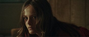 Movie still from “Adoration” (2019), directed by Fabrice du Welz – A woman with long brown hair sitting in front of a wooden wall; Close Up shot, Over the shoulder angle