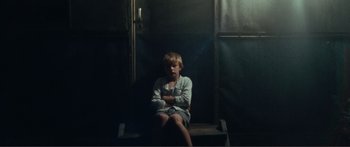 Movie still from “Adoration” (2019), directed by Fabrice du Welz – A young boy sitting on steps in a dark room; Wide shot, High angle