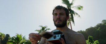 Movie still from “Adrift” (2018), directed by Baltasar Kormákur – A man holding a camera in front of palm trees; Close Up shot, Low angle