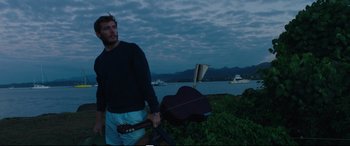 Movie still from “Adrift” (2018), directed by Baltasar Kormákur – A man standing next to a body of water holding a guitar; Medium shot, Low angle