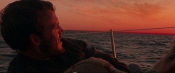 Movie still from “Adrift” (2018), directed by Baltasar Kormákur – A man sitting on the back of a sailboat at sunset; Close Up shot, Over the shoulder angle
