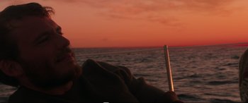 Movie still from “Adrift” (2018), directed by Baltasar Kormákur – A person sitting on the beach at sunset; Medium shot, Low angle