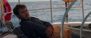 Movie still from “Adrift” (2018), directed by Baltasar Kormákur – A man sitting on the back of a sailboat in the water; Medium shot, High angle