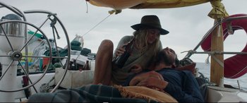 Movie still from “Adrift” (2018), directed by Baltasar Kormákur – A woman holding a bottle of beer next to a man laying on the ground; Medium shot, High angle