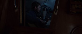 Movie still from “Adrift” (2018), directed by Baltasar Kormákur – A man sitting in front of a microphone in front of a window; Medium shot, Over the shoulder angle