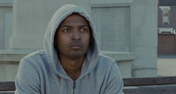 Movie still from “Adulthood” (2008), directed by Noel Clarke – A man wearing a gray hooded sweatshirt sitting in front of a wall; Close Up shot, Low angle