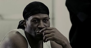 Movie still from “Adulthood” (2008), directed by Noel Clarke – A man with a black hat is leaning on his hand; Close Up shot, Over the shoulder angle