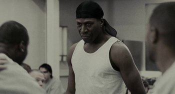Movie still from “Adulthood” (2008), directed by Noel Clarke – A man in a white tank top wearing a black hat; Close Up shot, Low angle