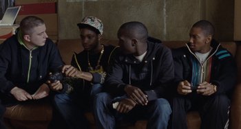 Movie still from “Adulthood” (2008), directed by Noel Clarke – A group of young men sitting on a couch holding wii remotes; Medium shot, Over the shoulder angle