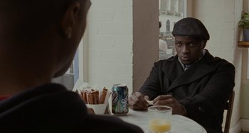 Movie still from “Adulthood” (2008), directed by Noel Clarke – Two men sitting at a table with a can of soda; Medium shot, Over the shoulder angle