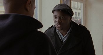 Movie still from “Adulthood” (2008), directed by Noel Clarke – A man wearing a hat talking to another man in front of a window; Close Up shot, Over the shoulder angle