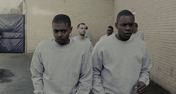 Movie still from “Adulthood” (2008), directed by Noel Clarke – A group of men standing next to each other in front of a brick wall; Medium shot, Over the shoulder angle