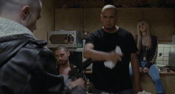 Movie still from “Adulthood” (2008), directed by Noel Clarke – A man in a black t - shirt is holding a white object; Medium shot, Over the shoulder angle