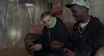 Movie still from “Adulthood” (2008), directed by Noel Clarke – Two young men sitting on a couch playing a video game; Medium shot, Low angle