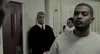 Movie still from “Adulthood” (2008), directed by Noel Clarke – A man in a prison uniform standing in front of another man; Close Up shot, Over the shoulder angle