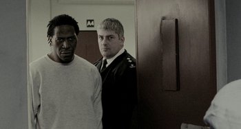 Movie still from “Adulthood” (2008), directed by Noel Clarke – Two men standing next to each other in front of a door; Medium shot, Over the shoulder angle