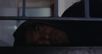 Movie still from “Adulthood” (2008), directed by Noel Clarke – A man in a black hoodie peeking out from behind a metal fence; Close Up shot, Overhead angle