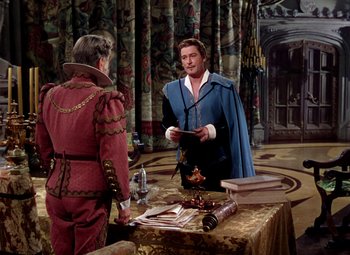 Movie still from “Adventures of Don Juan” (1948), directed by Vincent Sherman – A man in a blue and red suit standing next to another man in a red and blue suit; Medium shot, Over the shoulder angle