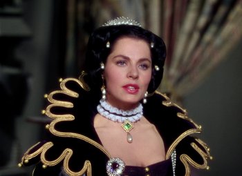 Movie still from “Adventures of Don Juan” (1948), directed by Vincent Sherman – A woman in a black and gold dress with a tiara and necklace; Close Up shot, Over the shoulder angle