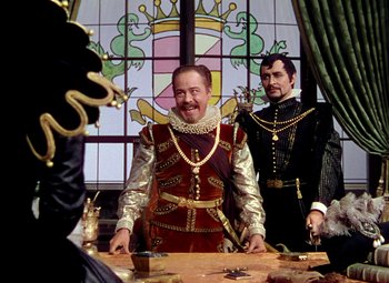 Movie still from “Adventures of Don Juan” (1948), directed by Vincent Sherman – Two men dressed in renaissance clothing standing in front of a stained glass window; Medium shot, Over the shoulder angle