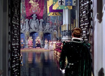 Movie still from “Adventures of Don Juan” (1948), directed by Vincent Sherman – A man in a green suit standing in front of a group of people; Wide shot, Over the shoulder angle