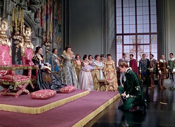 Movie still from “Adventures of Don Juan” (1948), directed by Vincent Sherman – A man kneeling down in front of a group of people; Wide shot, High angle