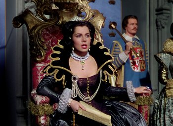 Movie still from “Adventures of Don Juan” (1948), directed by Vincent Sherman – A woman sitting on a throne with a man standing behind her; Medium shot, Low angle