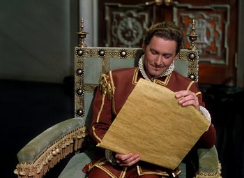 Movie still from “Adventures of Don Juan” (1948), directed by Vincent Sherman – A man sitting in a chair holding a piece of paper; Medium shot, High angle