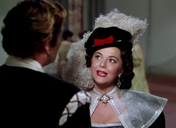 Movie still from “Adventures of Don Juan” (1948), directed by Vincent Sherman – A person wearing a hat and a dress; Close Up shot, Over the shoulder angle