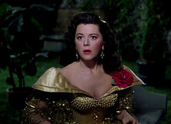 Movie still from “Adventures of Don Juan” (1948), directed by Vincent Sherman – A woman in a gold dress with a red flower in her hair; Close Up shot, High angle