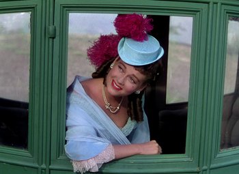 Movie still from “Adventures of Don Juan” (1948), directed by Vincent Sherman – A woman wearing a blue hat looking out of a window; Medium shot, Low angle