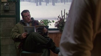 Movie still from “Affliction” (1997), directed by Paul Schrader – A man sitting on a bench reading a magazine; Medium shot, Over the shoulder angle