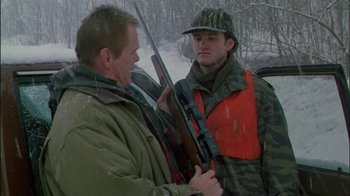 Movie still from “Affliction” (1997), directed by Paul Schrader – A man holding a rifle talking to another man in the snow; Medium shot, Over the shoulder angle