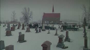 Movie still from “Affliction” (1997), directed by Paul Schrader – A cemetery with a church in the background; Extreme Wide shot, High angle