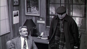 Movie still from “Affliction” (1997), directed by Paul Schrader – Two men are standing in front of a no smoking sign; Medium shot, Over the shoulder angle