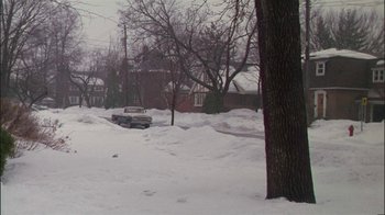 Movie still from “Affliction” (1997), directed by Paul Schrader – A car is parked in the middle of a snowy street; Extreme Wide shot, High angle