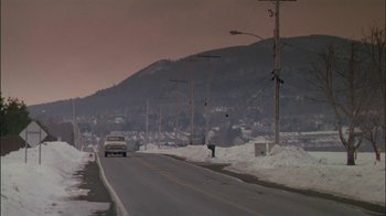 Movie still from “Affliction” (1997), directed by Paul Schrader – A car driving down a street near a mountain; Extreme Wide shot, High angle