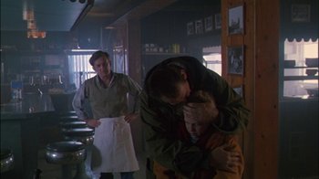 Movie still from “Affliction” (1997), directed by Paul Schrader – A man and a woman hug in a kitchen; Medium shot, Over the shoulder angle