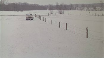 Movie still from “Affliction” (1997), directed by Paul Schrader – A car driving down a snow covered road near barbed wire fence; Extreme Wide shot, High angle