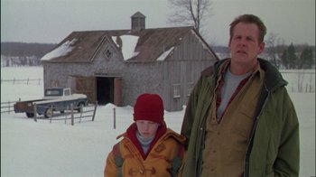 Movie still from “Affliction” (1997), directed by Paul Schrader – A man and a boy standing next to each other in a field; Medium shot, Low angle