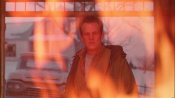 Movie still from “Affliction” (1997), directed by Paul Schrader – A man standing in front of a window with a fire behind him; Close Up shot, Low angle
