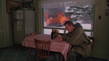 Movie still from “Affliction” (1997), directed by Paul Schrader – A man sitting at a dining room table in front of a fire; Wide shot, High angle