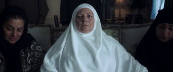 Movie still from “After Love” (2020), directed by Aleem Khan – An older woman wearing a head covering sitting in a chair; Close Up shot, Low angle