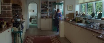 Movie still from “After Love” (2020), directed by Aleem Khan – A woman standing in a kitchen next to an open door; Wide shot, High angle