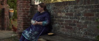 Movie still from “After Love” (2020), directed by Aleem Khan – A woman sitting on top of a bench holding a cup; Medium shot, Over the shoulder angle