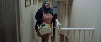 Movie still from “After Love” (2020), directed by Aleem Khan – A woman carrying a basket of food down the stairs; Medium shot, Low angle