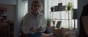 Movie still from “After Love” (2020), directed by Aleem Khan – A woman standing in a room holding a pair of scissors; Medium shot, Over the shoulder angle