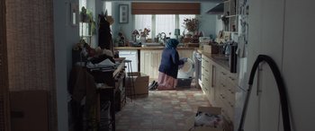 Movie still from “After Love” (2020), directed by Aleem Khan – A woman in a kitchen washing dishes in a sink; Wide shot, Over the shoulder angle